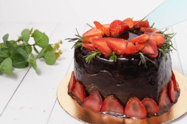 Yemek ve fırın konsepti için beyaz arka planda çilekli lezzetli çikolatalı pastayı kesen plastik bir bıçak.