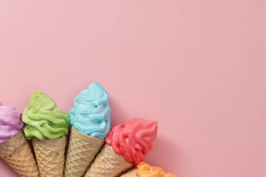 Tatlı ve ferahlatıcı tatlı konsepti için pembe arka planda çeşitli renkli kremalı dondurma külahları