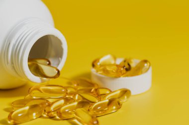 Omega-3 balık yağı kapsülleri sarı arka planda, sağlık konsepti için.