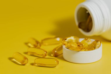 Omega-3 balık yağı kapsülleri sarı arka planda, sağlık konsepti için.