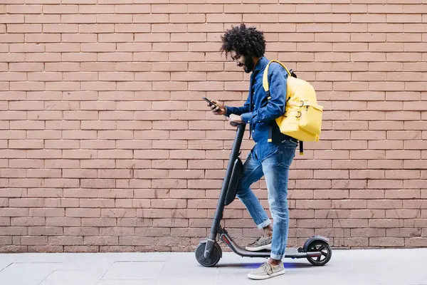 Jongeman Met Rugzak Scooter Voor Bakstenen Muur Kijkend Naar Mobiele — Stockfoto