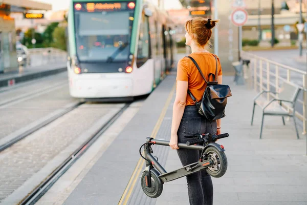 Widok Tyłu Kobiety Plecakiem Składanym Skuterem Elektrycznym Czekającej Przystanku Tramwajowym — Zdjęcie stockowe