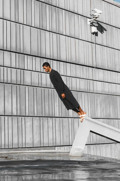 Молодий Чоловік Чорному Кафтані Стоїть Плиткою Бетонній Конструкції Відкритому Повітрі — стокове фото