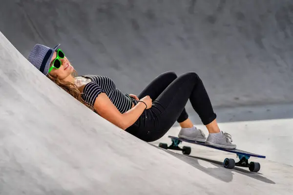 スケートボードを持つ若い女性はスケートパークに横たわっている — ストック写真
