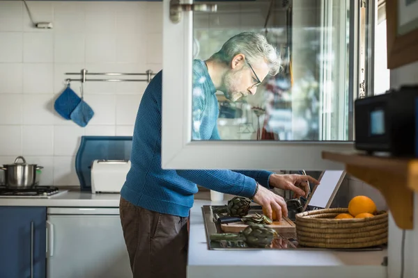 Homem Maduro Preparando Alcachofra Sua Cozinha Usando Tablet Digital — Fotografia de Stock