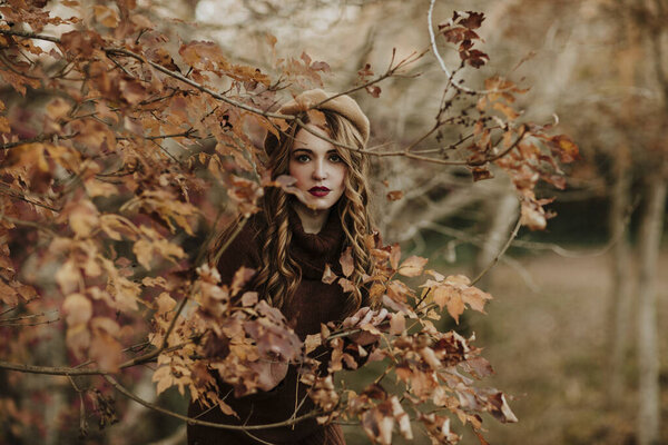 Portrait of fashionable woman standing behind autumn leaves