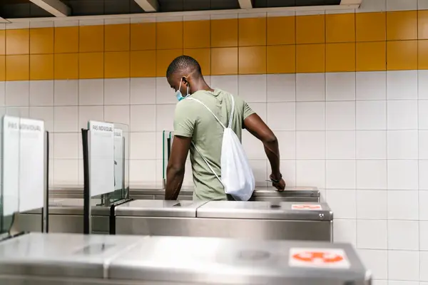 若いです男身に着けていますマスクでバックパックを歩くターンスタイルで地下鉄駅 — ストック写真