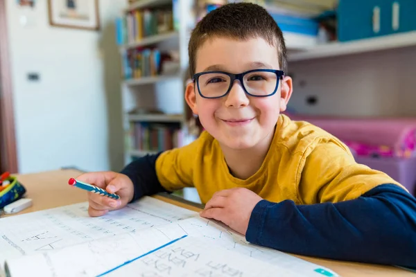 Sonriente Chico Lindo Sentado Con Libro Escritorio Durante Educación Casa — Foto de Stock