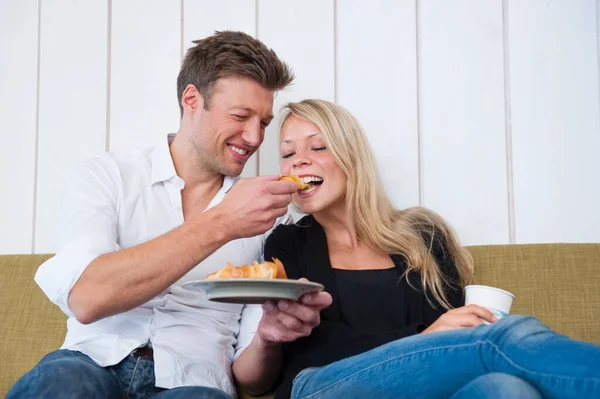 Sonriente Hombre Alimentación Croissant Novia Mientras Sentado Sofá Casa —  Fotos de Stock