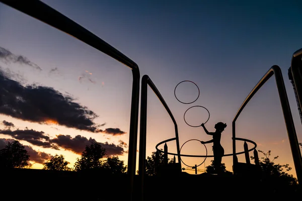 夕阳西下 轮廓细腻的女运动员在天空中抛接塑料圈圈 — 图库照片