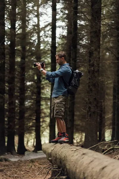 Mężczyzna Turysta Fotografuje Aparatem Podczas Stojąc Logu Lesie — Zdjęcie stockowe