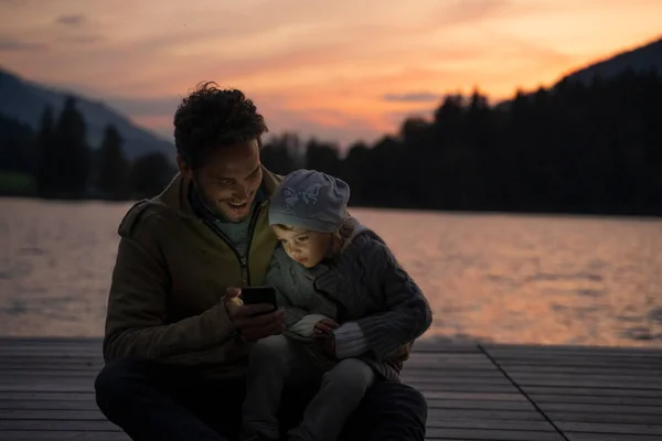 Father Little Daughter Playing Smart Phone Lakeshore Jetty Dusk — Stock Photo, Image