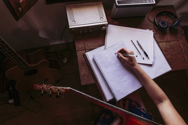 Jovem Mulher Escrevendo Livro Enquanto Pratica Guitarra Casa — Fotografia de Stock