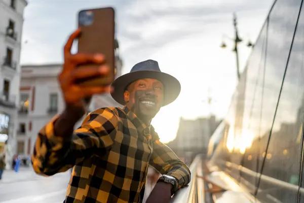 Uśmiechnięty Afrykanin Fotografujący Przez Smartfon Stojąc Mieście Podczas Zachodu Słońca — Zdjęcie stockowe