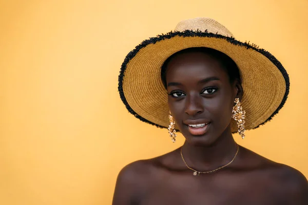 黄色の壁に立っている間に帽子をかぶっている若い女性 — ストック写真