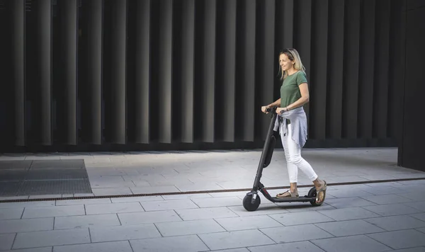 Kvinde Stående Elektrisk Push Scooter Mod Metal Væg Solrig Dag - Stock-foto