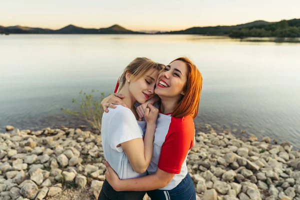 Mulher Feliz Abraçando Namorada Enquanto Junto Lago Durante Pôr Sol — Fotografia de Stock