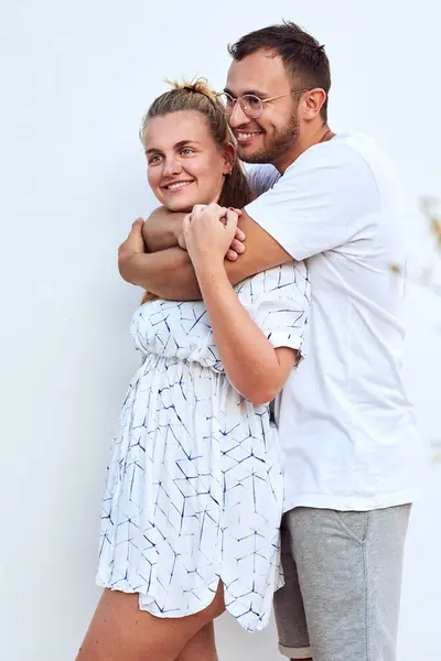 Lächelndes Junges Paar Schaut Weg Während Vor Weißer Wand Steht — Stockfoto