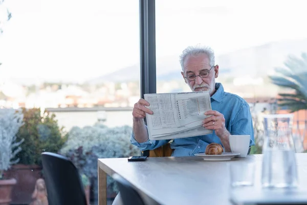 Homem Sênior Lendo Jornal Enquanto Sentado Mesa Casa — Fotografia de Stock