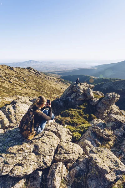 Young Woman Photographing Male Friend Sitting Mountain Clear Sky — Stock Photo, Image