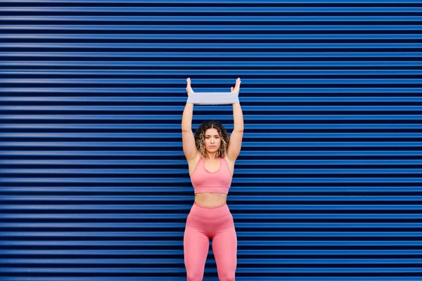 手拿着抵抗带的女运动员在蓝墙前锻炼 — 图库照片
