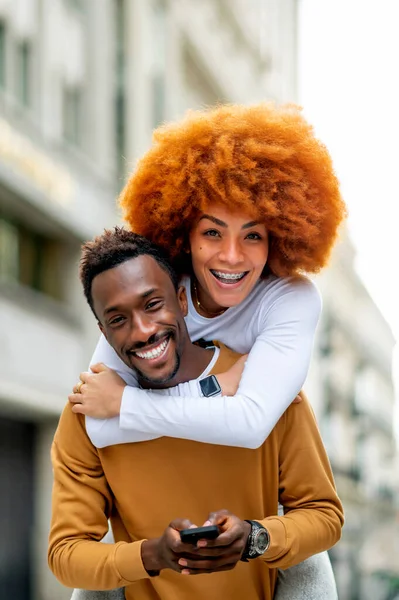 Smiling Woman Piggybacking Man Using Mobile Phone While Standing Outdoors — Stock Photo, Image