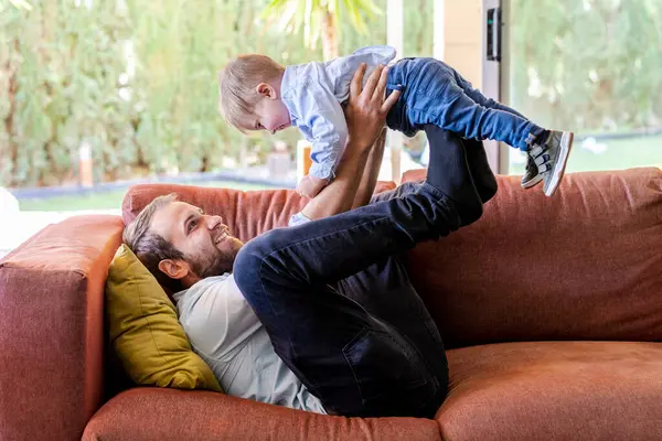 Sorrindo Pai Levantando Filho Enquanto Deitado Sofá Sala Estar — Fotografia de Stock