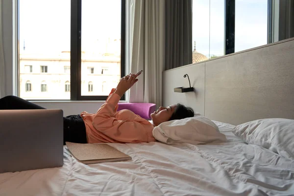 Profesjonalne Wiadomości Tekstowe Dla Kobiet Pośrednictwem Smartfona Leżącego Łóżku Hotelu — Zdjęcie stockowe