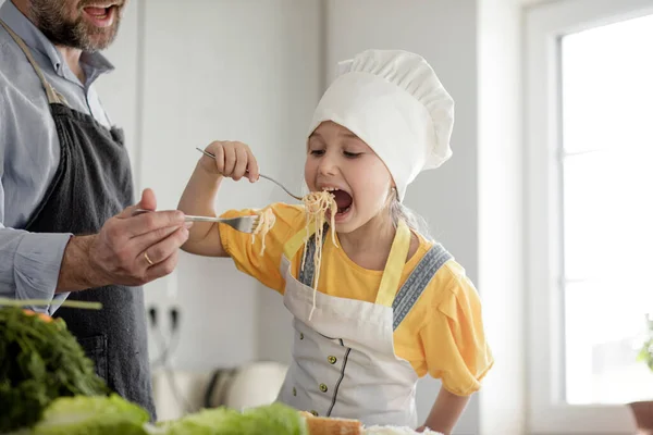 Girl Wearing Apron Chef Hat Eating Noodles Father While Standing — Stock Photo, Image
