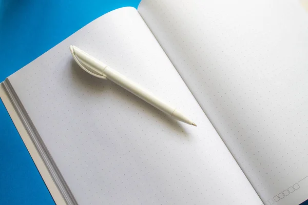 The pen rests on an unfolded notebook. Blank sheet and pen for writing.