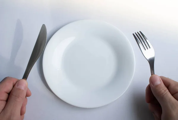 Fork and knife in hand against the background of an empty plate. A man in a restaurant. Food stocks are out. No food. Dinner is eaten. At an empty table with a fork and knife.