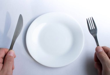 Boş bir tabağın arka planında çatal ve bıçak var. Restoranda bir adam. Yiyecek stokları bitti. Yemek yok. Akşam yemeği yendi. Çatal ve bıçakla boş bir masada..