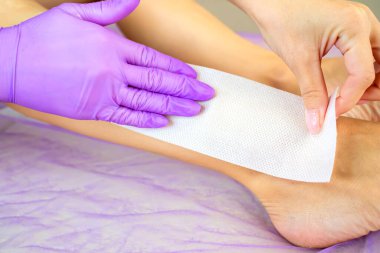 Balmumu tüyü. Balmumu şeritli epilasyon. Bacaklarda saç kesimi. Eldivenli el ve balmumu şerit.