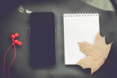 Sonbahar şarkı listesi. Sonbaharın arka planında telefon ve not defteri. Akçaağaç yaprağı ve boş defter. Sonbahar dönemi hakkında şiirler. Kulaklık ve telefon..