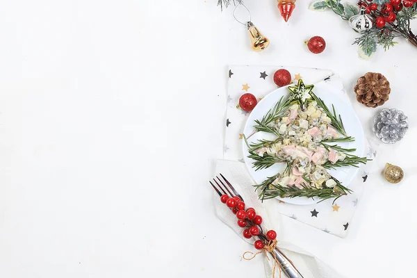 Christmas new year food, traditional festive olivier salad with fir branches and cones and decorations on a light table, idea for food design, place for recipe, flat lay, selective focus