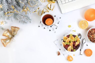 Modern kadın çalışma masası, sağlıklı kahvaltı, ev ofisi. Bilgisayar, Noel süslemeleri, meyve salatası ve bir fincan çay. Yaşam tarzı konsepti, düz yatış