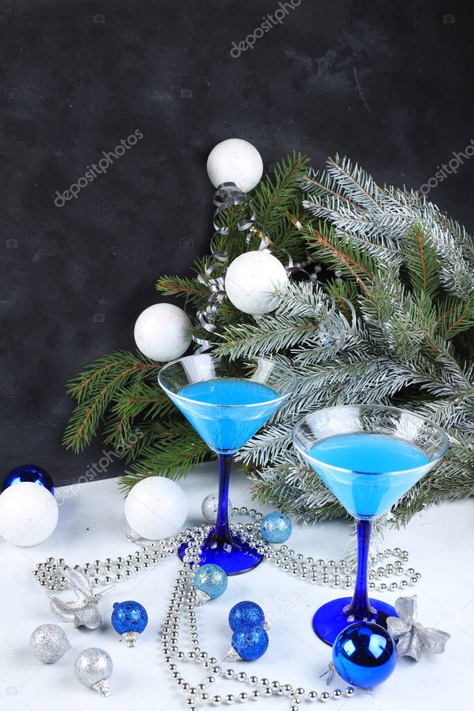 Blue alcoholic cocktail with lemonade, champagne or martini in glasses on a festive christmas table with fir branches and decorations, bar concept, spirits at a party, selective focus