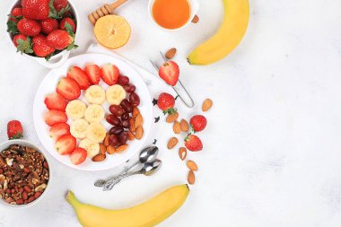 Malzemelerden oluşan faydalı bir kahvaltı müsli çilekli yoğurt, üzümler, parlak bir masada muz ve bal, meyve salatası. Sağlıklı ve doğal gıda konsepti, yaşam tarzı, çocuklar için yiyecek, seçici odaklanma