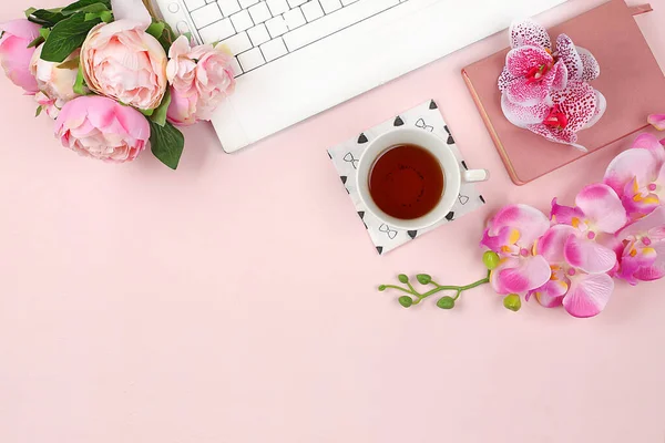 Modern woman working desk, home office. Computer, a cup of tea, macaroons and spring orchid flowers on a light table. Business minimal concept, home comfort, top view, flat lay, place for text, selective focus