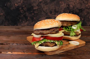 İki duble çizburger taze marul yapraklı, domates, krem peynir, soğan ve pirzola eski bir tahta üzerinde, yemek teslimatı, kafe, restoran, menü, seçici odaklı.