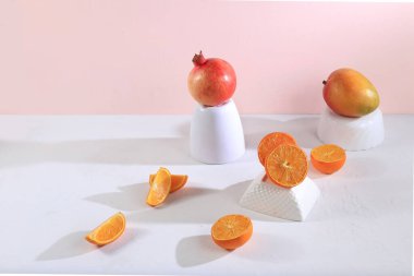 Turunçgil, portakal suyu ve portakal suyu, nar ve mango içeren modern yaşam ve pembe arka planda uzun sert gölgeli podyumlar, minimum detoks diyeti konsepti, yaz vitamini içecekleri, seçici odaklanma