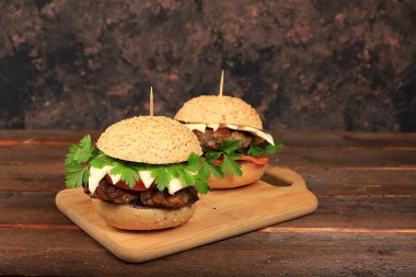 Taze maydanoz yapraklı iki çizburger, domates, krem peynir, soğan ve pirzola eski bir ahşap tahta üzerinde, yemek teslimatı, bir kafe reklamı, restoran, menü, sade anahtar, seçici odaklanma