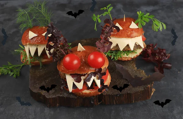 Halloween food concept. Scary burgers with fresh parsley leaves, tomatoes, cream cheese, onion and cutlet on old concrete background, low key, food delivery, cafe advertisement, menu, selective focus,