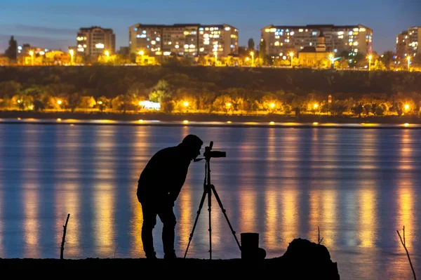 Photographer silhouette in the night with water and city on background. Night photography