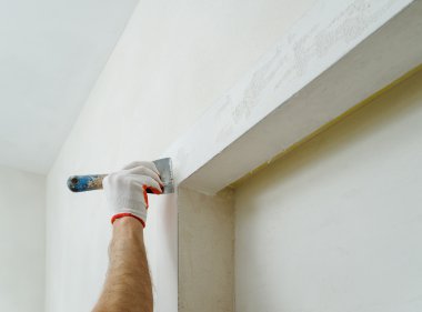 Dekoratif alçı kaplama. Adam bir spatula kullanarak duvar üzerinde dağınık doku yapar.