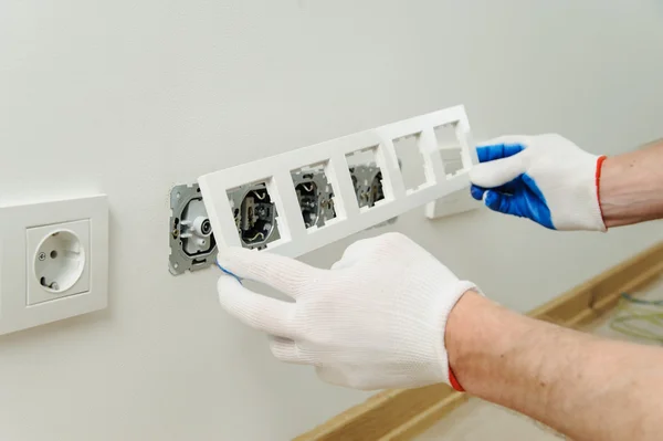 The electrician installs a decorative frame on electric and TV sockets.