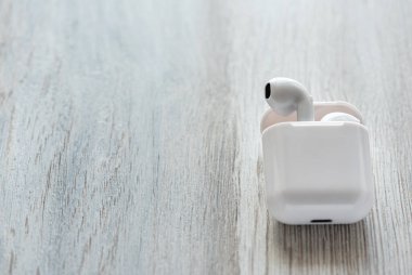 Tahta bir arka planda şarj çantasında beyaz kablosuz kulaklık..