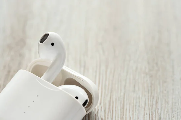 White wireless headphones in a charging case on a wooden background.