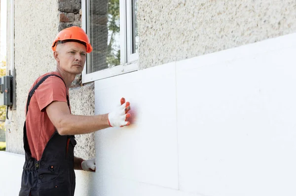 Insulation of the house with polyfoam. The worker is installing a styrofoam board on the facade.