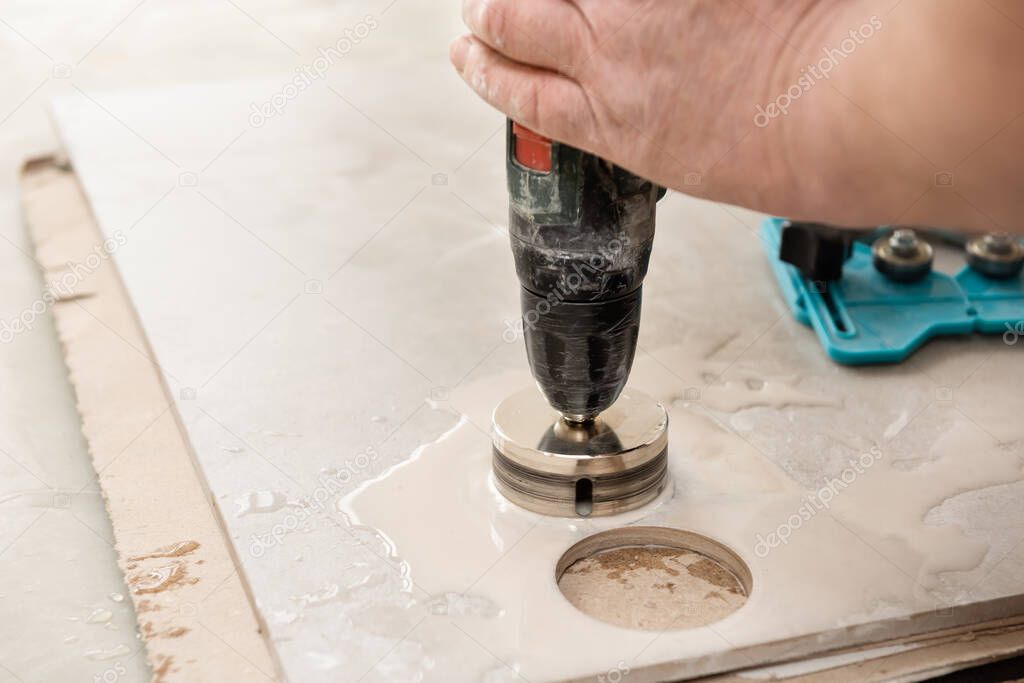 A tiler is using a diamond crown to drill holes in the ceramic tile.